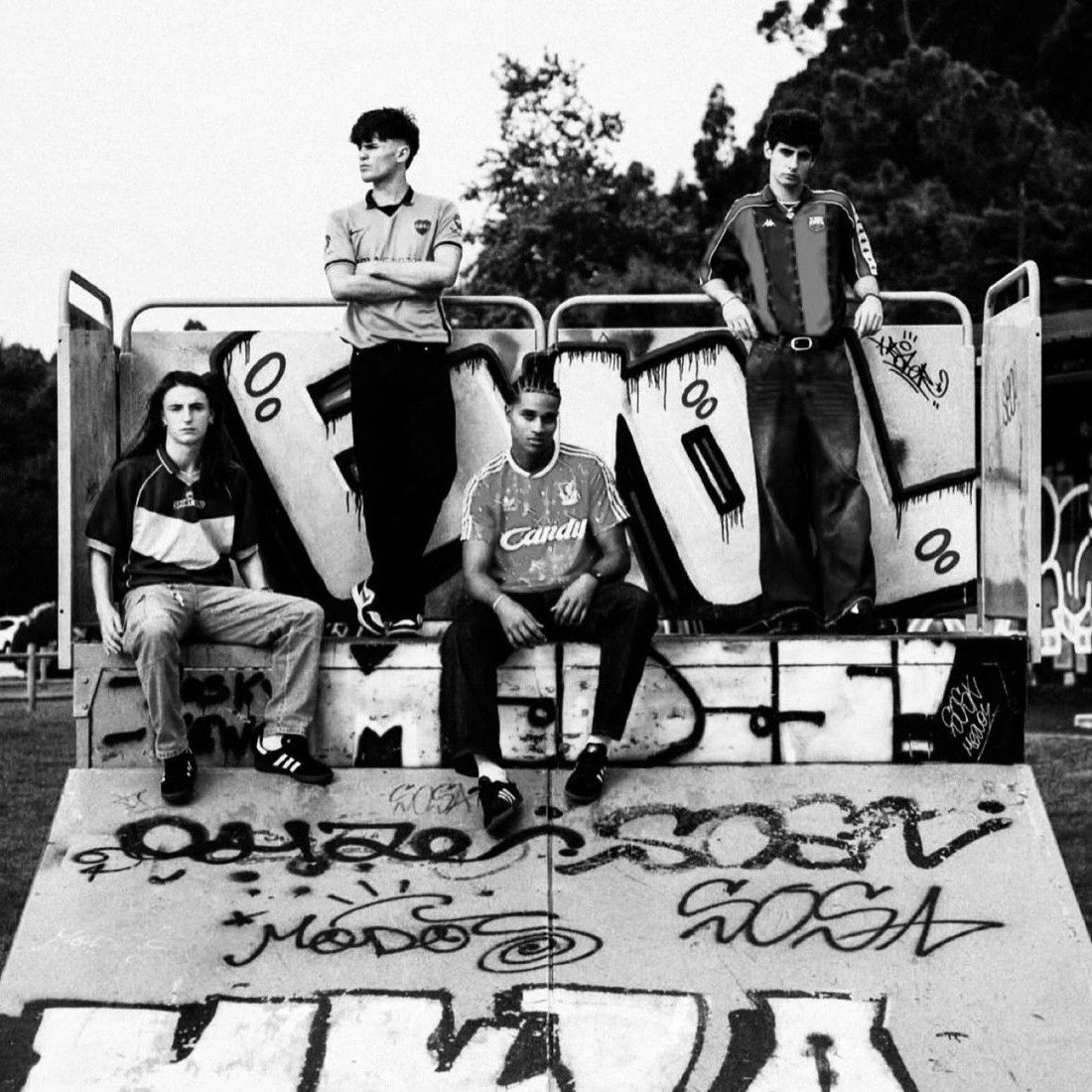 Cuatro chicos con cortes de 2Barbers posando en un skatepark con grafitis